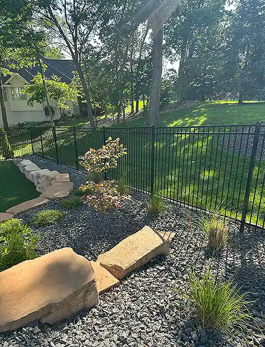 A black fence borders a lawn with a stone terrace garden.