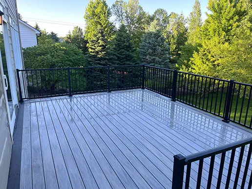 A freshly pressure-washed deck surrounded by a black fence.