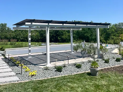 A modern black-and-white pergola adds shade and a decorative touch to a grassy area with a stone walkway.